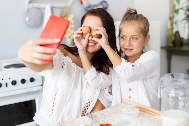 Happy mother and daughter taking selfies with eggs