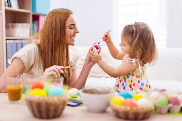 Happy mother helping baby painting on easter eggs