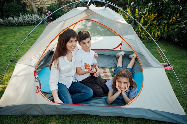 Happy mother with her daughter and son in tent on grass at park