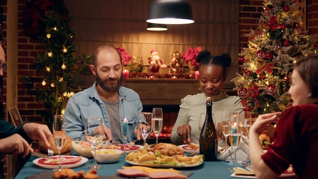 Happy multiethnic family gathered around Christmas dinner table enjoying traditional home cooked food. Festive relatives sitting at home while celebrating winter holiday together.