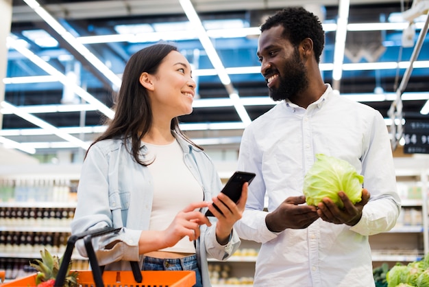 Happy multiracial couple choosing goods and looking at each other in supermarket