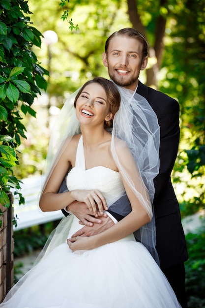 Happy newlyweds smiling, embracing, posing in park.