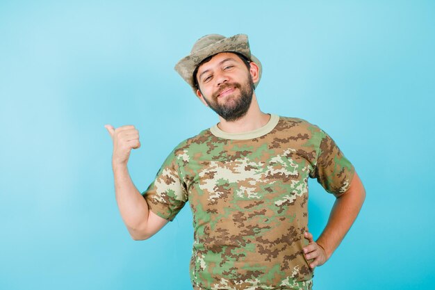 Happy officer is showing back with thumb and putting other hand on waist on blue background