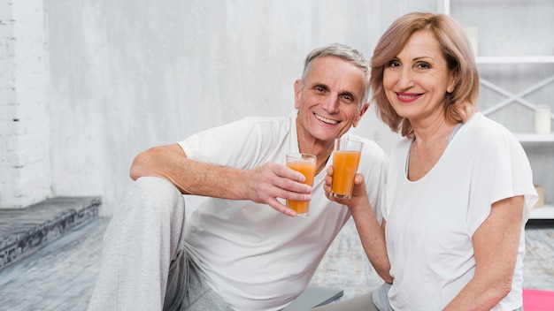 Happy old couple sitting at home holding glass of juice