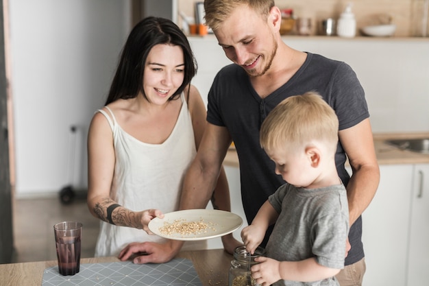 Happy parents looking at little boy removing oats from the jar into plate