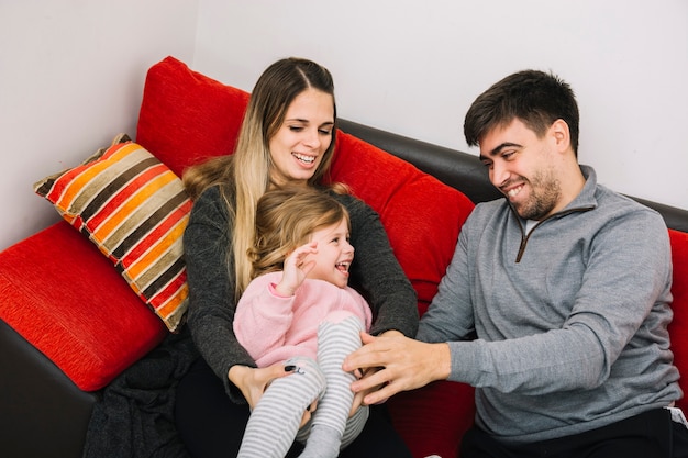 Free photo happy parents sitting on sofa playing with their daughter