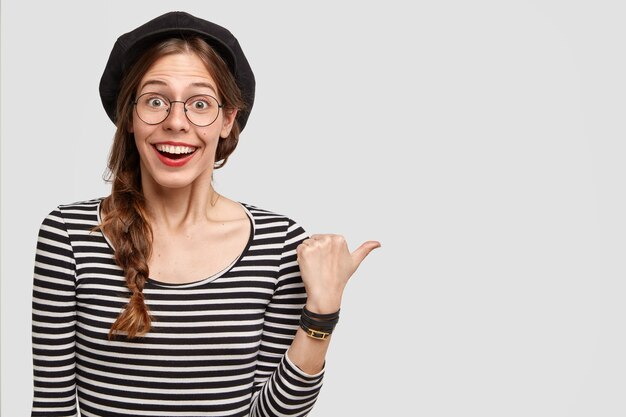 Happy Parisian woman with positive smile, indicates aside