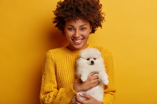 happy pet owner being in good mood after visiting vet with puppy, finds out her spitz dog is healthy, wears yellow knitted sweater