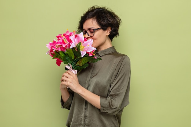 Happy and pleased woman with short hair holding bouquet of flowers and smelling