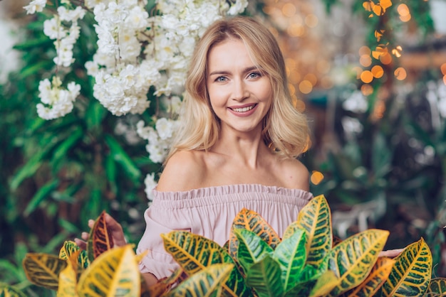 Free photo happy portrait of a blonde young woman standing in front of yellow and green leaves