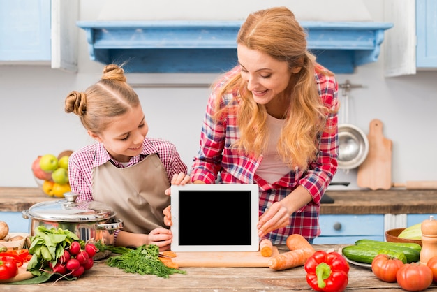 Happy portrait of mother and daughter looking at digital tablet on wooden desk