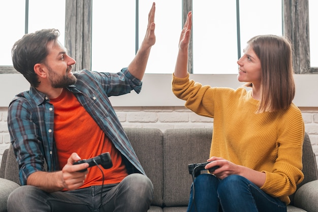 Free Photo happy portrait of a young couple sitting on sofa giving high five to each other while playing video game