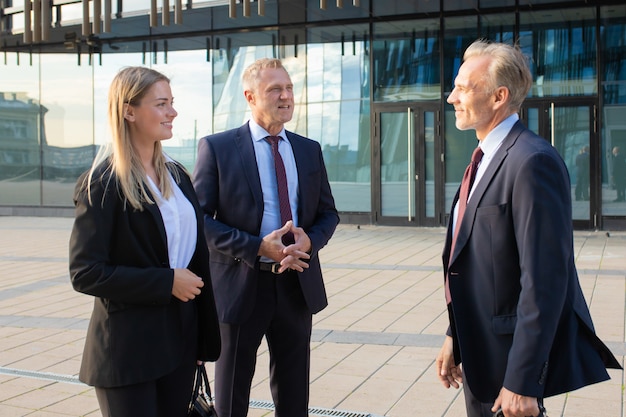 Free Photo happy positive business partners meeting at office building, standing and talking outdoors, discussing deal. medium shot, side view. cooperation concept