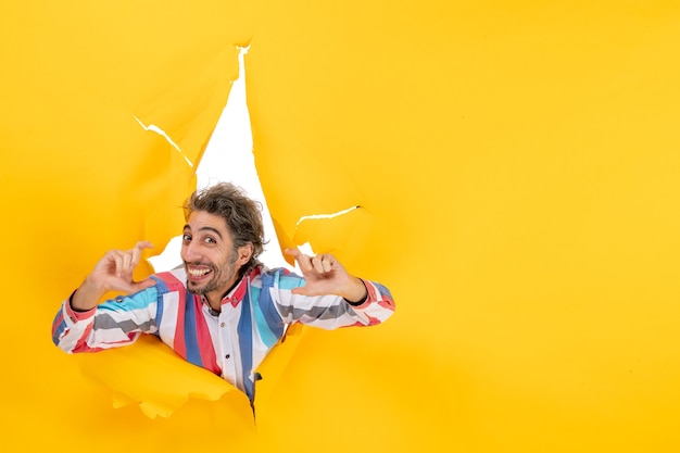 Free photo happy positive and emotional bearded guy in a torn hole and free background in yellow paper