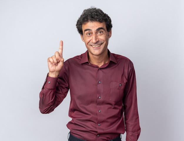 Happy and positive senior man in purple shirt looking at camera smiling cheerfully pointing