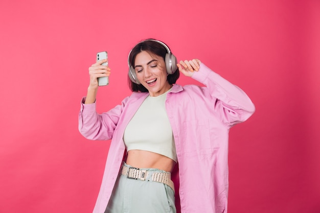 Happy positive woman in headphones on pink red wall