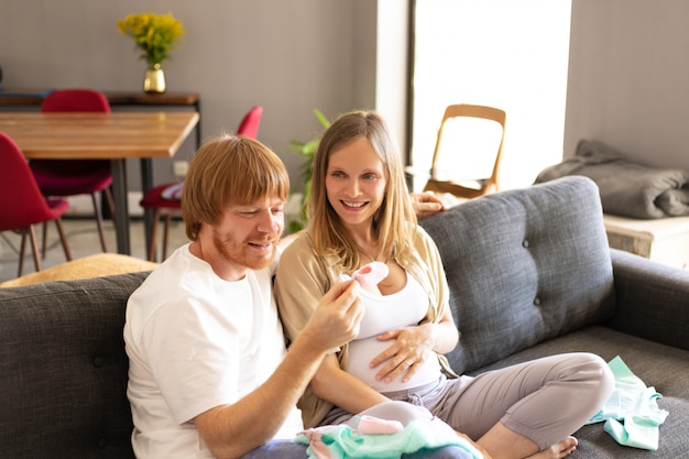 Free Photo happy pregnant couple checking baby clothes in living room