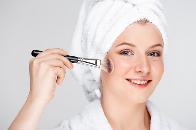 Happy pretty woman apply makeup with brush, wear bath towel