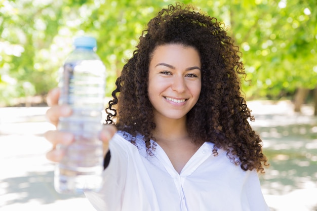 Happy pretty young woman showing water bottle in park