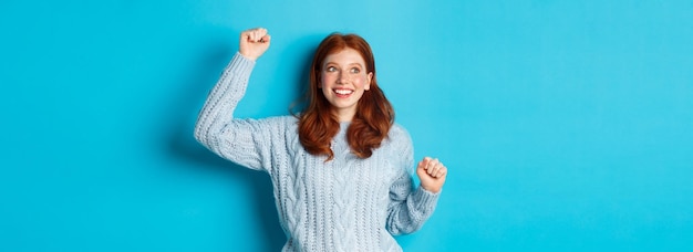 Happy redhead girl rooting for team cheering with raised hand and smiling celebrating victory or suc