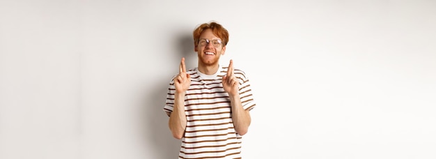 Free photo happy redhead man with bristle cross fingers for good luck and smiling hopeful making wish standing