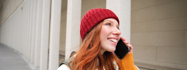 Free Photo happy redhead woman girl with phone talks has conversation on mobile app uses internet to call