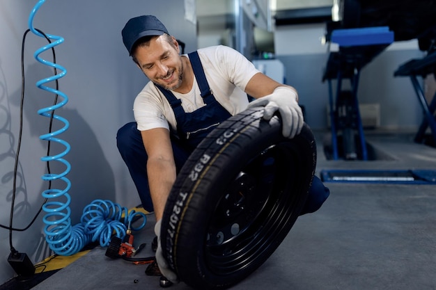 Free Photo happy repairman checking car tire at service workshop