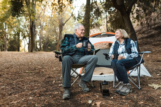 Happy retired couple having coffee by the tent in the forest