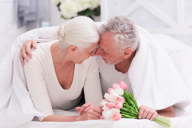 Happy romantic senior couple on bed holding tulip flowers in hand