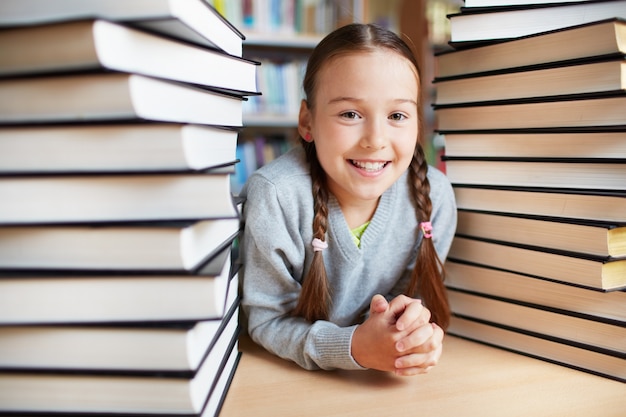 Free photo happy schoolgirl surrounded with piles of books