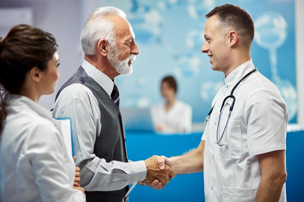 Happy senior businessman and doctor shaking hands while greeting in a hallway at the hospital