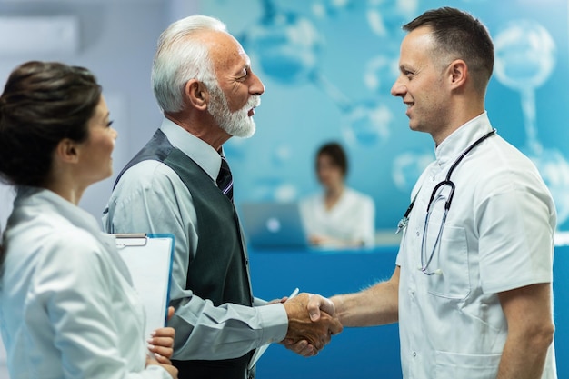 Free photo happy senior businessman and male doctor handshaking while greeting in a hallway at clinic