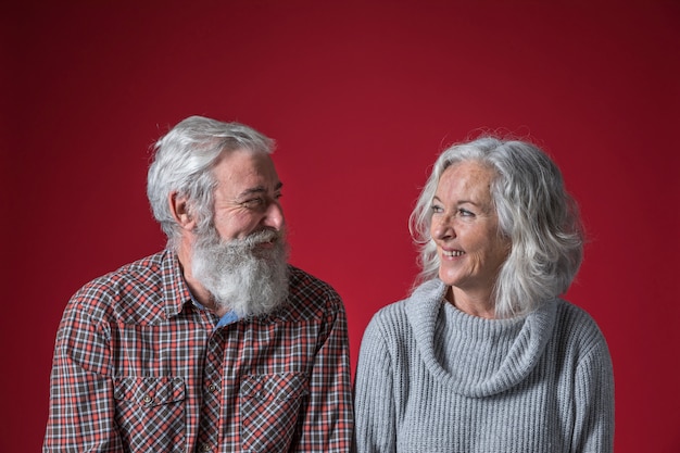 Happy senior couple looking to each other against red backdrop