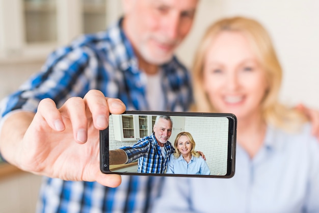 Free photo happy senior husband and wife are making selfie on mobile phone in kitchen