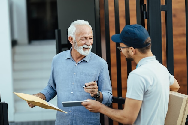 Happy senior man communicating with a deliverer while signing on digital tablet for home delivery