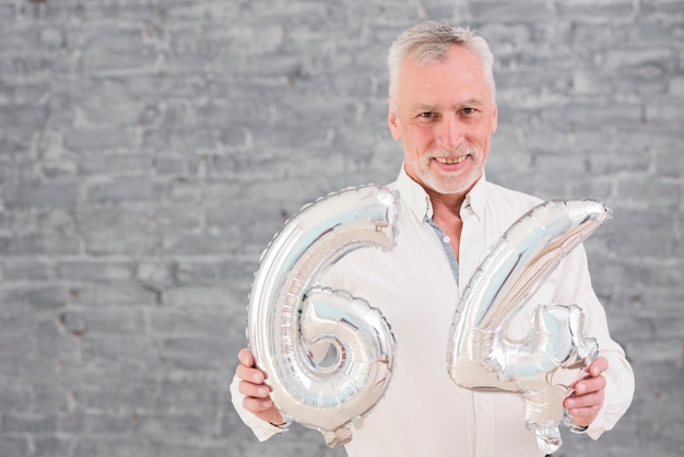 Free photo happy senior man holding silver foil balloon on his 64 birthday