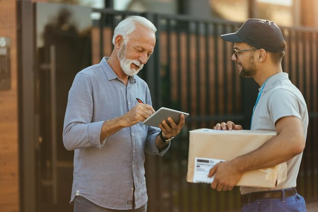 Happy senior man using touchpad and signing for a delivery from courier