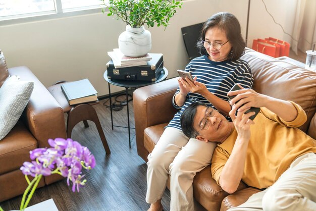 Free photo happy senior old asian lover couple holding smartphone looking at cellphone screen laughing casual relaxing sit on sofa together smiling elder mature grandparents family embracing lifestyle