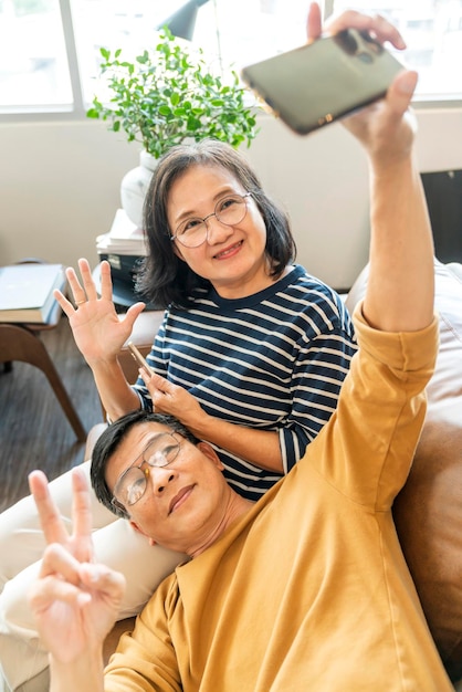 Free photo happy senior old asian lover couple holding smartphone looking at cellphone screen laughing casual relaxing sit on sofa together smiling elder mature grandparents family embracing lifestyle