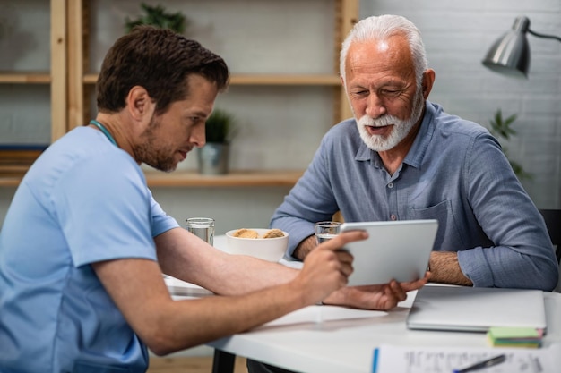 Free photo happy senior patient and his doctor looking at medical test results on touchpad during medical appointment