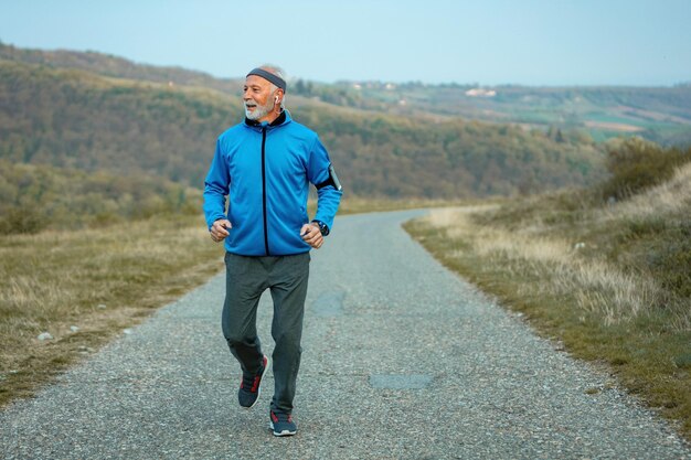 Happy senior sportsman feeling determined to keep up with active lifestyle and running on the road in nature Copy space