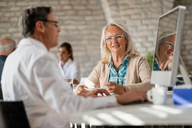 Free photo happy senior woman communicating with health care provider while he is analyzing medical data on a computer at clinic