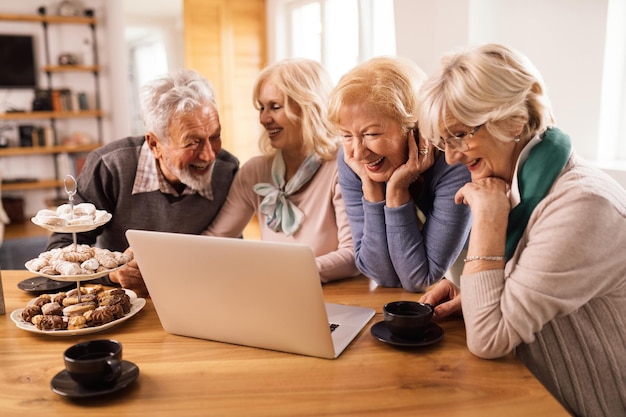 Happy senior woman and her friends having fun while surfing the Internet on computer at home