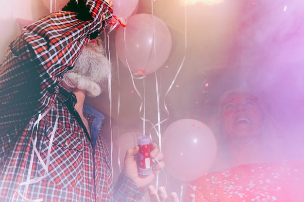 Free Photo happy senior woman looking at his husband blowing the bubble wand in the room filled with smoke