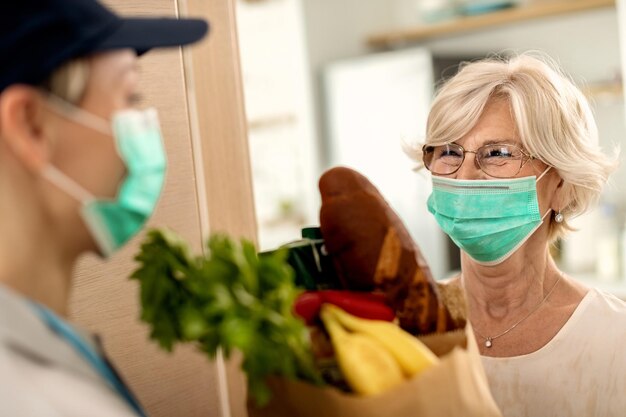 Happy senior woman with face mask receiving home delivery during coronavirus epidemic