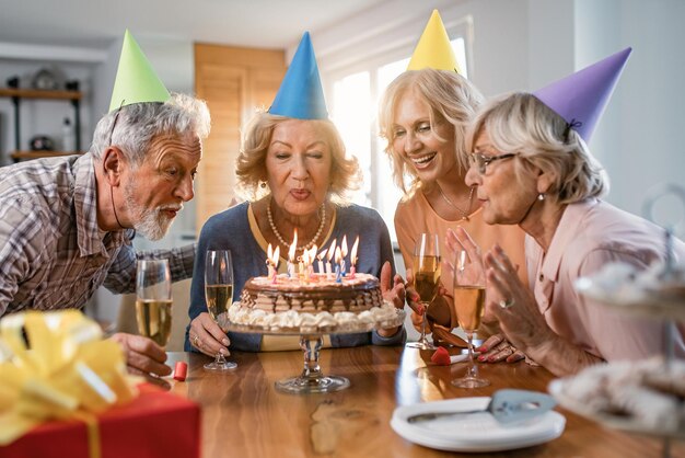 Happy seniors having fun while blowing candles on a cake during birthday party at home