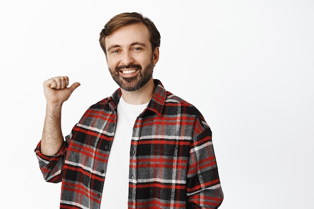 Happy simple guy smiling pointing right and showing advertisement standing in checked shirt over white background