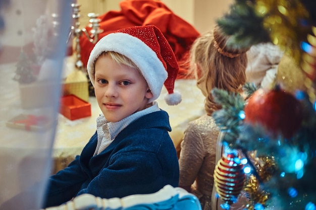 Happy sister and brother sitting at the table in an elegant living room decorated for Christmas.