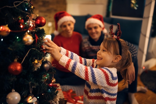 Happy small girl decorating Christmas tree in the evening at home