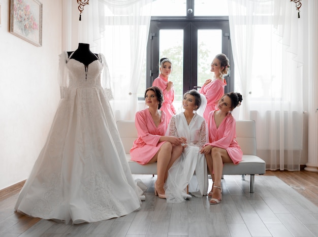 Free photo happy smiled bridesmaids with bride is looking on the wedding dress in light room, wedding preparation